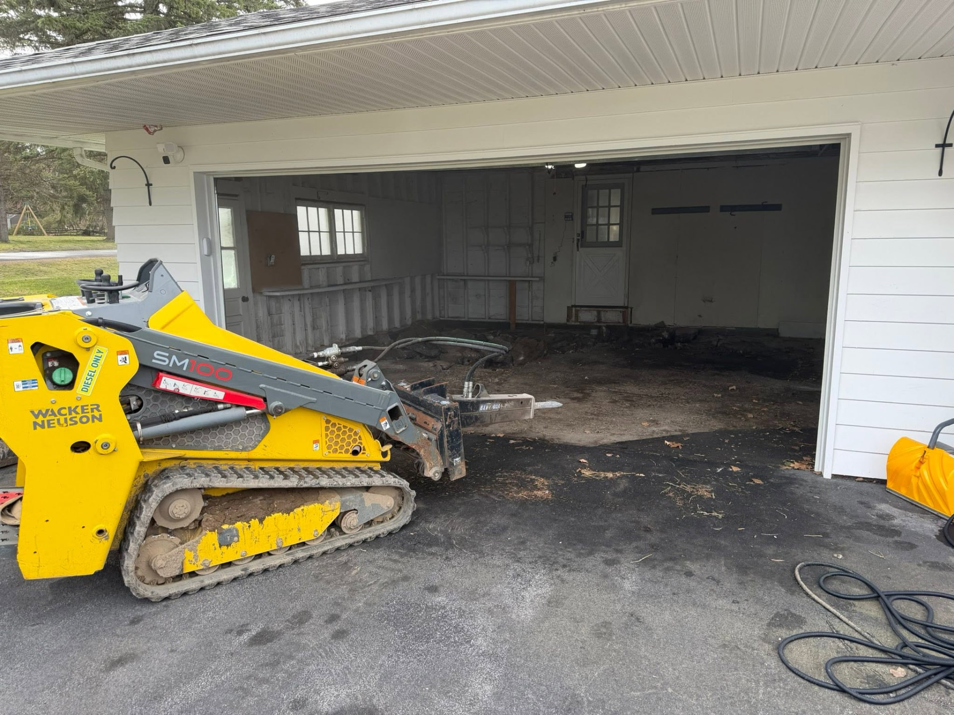 Track loader with hammer attachment breaking out a garage slab