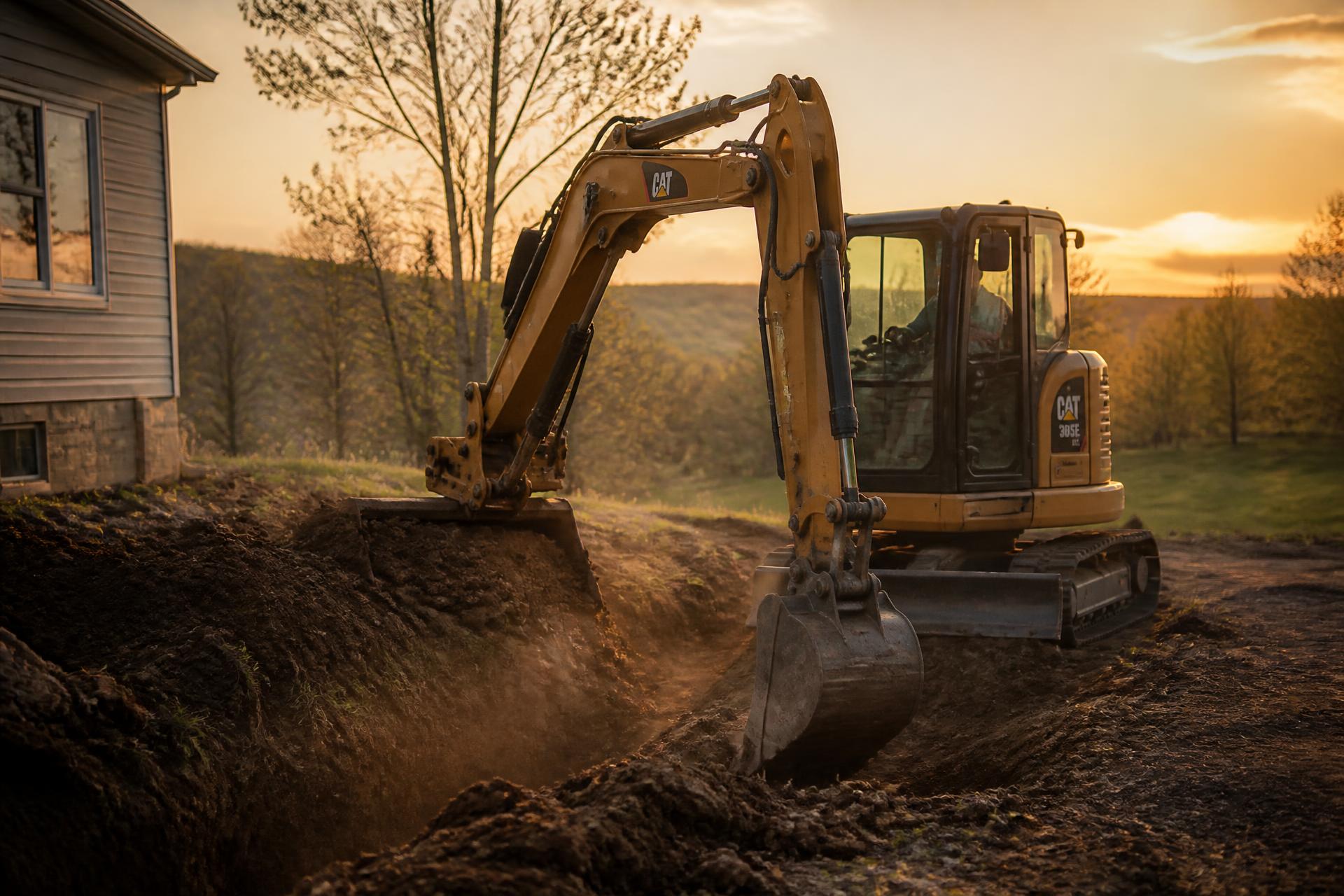 Excavator digging a trench beside a residential home at sunset